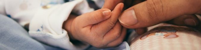 An adult hand holding a baby's hand