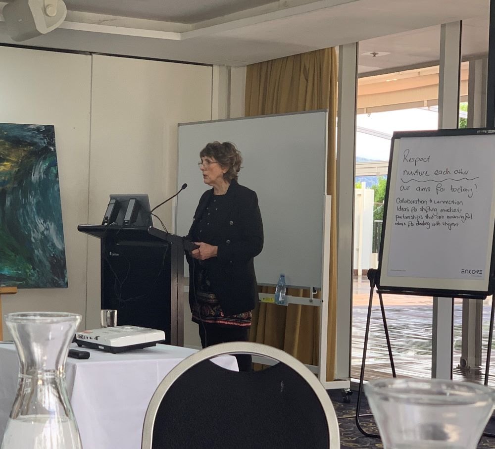 Coralie presenting at a workshop, standing at a lectern beside a whiteboard